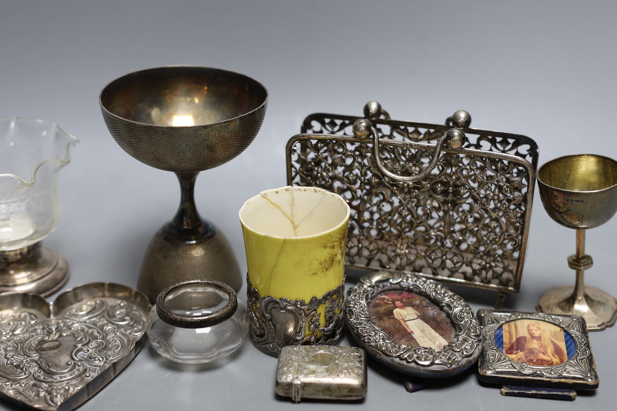 A small group of collectable items including a silver stationary rack, Laurence Emanuel, Birmingham, 1901, height 9.7cm, a silver communion goblet, silver mounted porcelain coffee cup, silver mounted glass vase, silver v